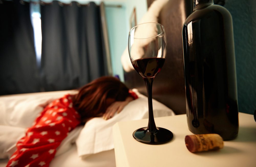 half full glass of wine on bedside table of early twenties woman in bed in a bedroom