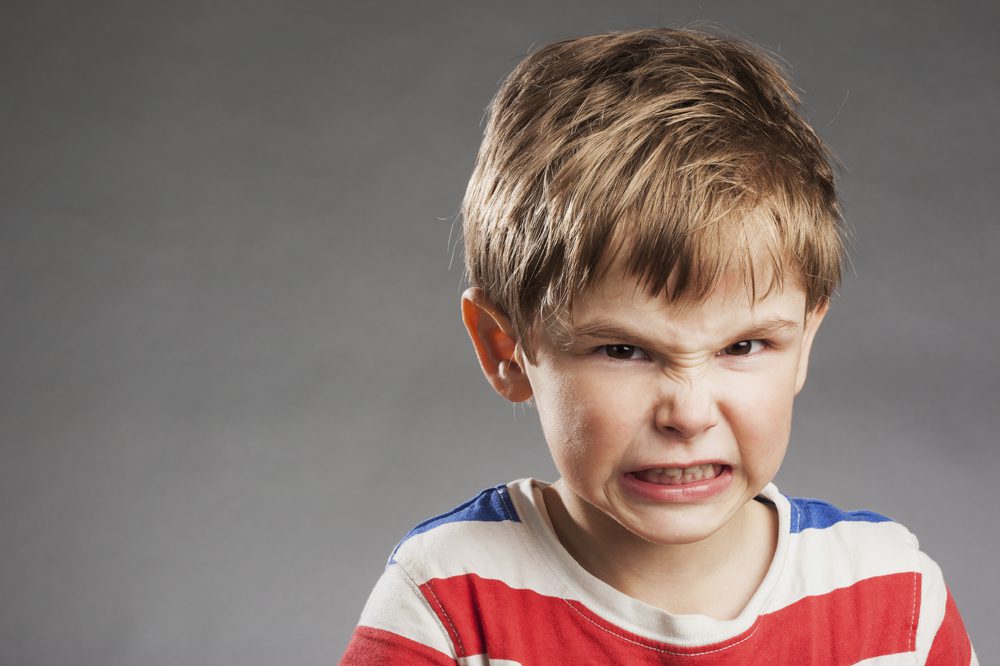 Young boy looking angry, clenching teeth against gray background